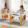 A young child is sitting at a child's activity table and chair set, drawing with a pencil. The table has books and storage compartments. The scene is set in a bright, well-lit room with a window in the background. Produktbild-Vorschau