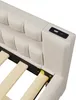 Close-up view of the headboard of a beige upholstered bed frame, showing a built-in USB charging port and wooden slats for the mattress support. Produktbild-Vorschau