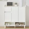 A white shoe cabinet with two doors, a drawer, and an open shelf at the bottom, displaying several pairs of shoes. A Marshall speaker and a desk calendar are on top. Produktbild-Vorschau