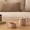 A tea set consisting of a teapot and a mug, placed on a wooden table in front of a couch. Podgląd zdjęcia produktu