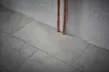 A close-up view of grey tiles and copper pipes against a textured wall. Produktbild-Vorschau