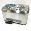 A stainless steel ice cream maker with a clear lid and digital display, shown on a white background with cleaning brushes. Náhled obrázku produktu