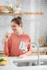 A woman drinks water in a kitchen, with a water filter attached to the faucet. Náhled obrázku produktu