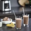 Two glasses of chocolate milkshake with straws, a bowl of chocolate ice cream, and a banana on a countertop. Voir les images du produit
