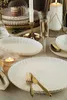 A table setting with white porcelain plates, gold cutlery, a champagne flute, and lit candles. Produktbild-Vorschau