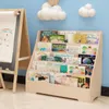A wooden bookshelf filled with children's books, next to an easel with a drawing on it, in a child's room. Produktbild-Vorschau