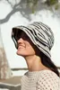 A woman wearing a crocheted hat and sweater outdoors. Produktbild-Vorschau