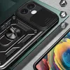 A close-up of a black smartphone case with a ring stand and camera cover, placed on a textured surface with a dark green background. Produktbild-Vorschau