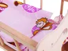 A close-up view of a doll's cradle with bedding featuring a monkey pattern. Náhľad obrázku produktu