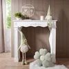 A white fireplace console decorated with gnomes, a plant, a candle, and a decorative sign. Produktbild-Vorschau