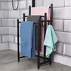 A black metal towel rack with four towels hanging on it, placed in a bathroom with tiled walls and a concrete floor. Náhľad obrázku produktu