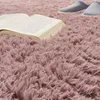 A close-up view of a fluffy pink rug with an open book and a pair of slippers on it. Produktbild-Vorschau