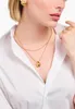 A woman wearing a white shirt and gold jewelry, including a necklace with a teardrop pendant, earrings, and rings. Anteprima dell’immagine prodotto