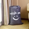 A large, gray laundry bag with a smiley face and the words 'wash me' printed on it, standing next to a beige curtain. Produktbild-Vorschau