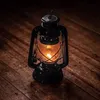A black kerosene lantern with a lit wick sits on a wooden surface. Náhľad obrázku produktu