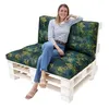 A woman is sitting on a pallet sofa with tropical-themed cushions. Náhled obrázku produktu