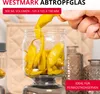 A hand is shown placing yellow pickled peppers into a clear glass jar with a gray base. Anteprima dell’immagine prodotto