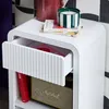 A white nightstand with an open drawer, displaying books, a candle, and a speaker. Produktbild-Vorschau