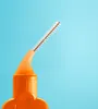 A close-up of an orange interdental brush with white bristles against a blue background. Produktbild-Vorschau