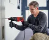 A man is using a red and black rotary hammer drill to drill into a concrete wall. Náhled obrázku produktu