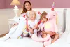 A woman and two children are sitting on a bed with large plush unicorn toys. Produktbild-Vorschau