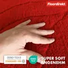 A hand is shown pressing into a soft, red bath mat, highlighting its texture and plushness. Logos and text indicating product features are present. Produktbild-Vorschau