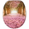 A toilet seat lid with a printed image of a pathway lined with trees and covered in pink flowers. Náhled obrázku produktu