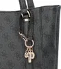 A close-up of a black Guess shopper bag with a repeating pattern and gold-colored charms hanging from a strap. Produktbild-Vorschau