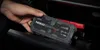 A hand is placing a jump starter into a car's storage compartment. Podgląd zdjęcia produktu