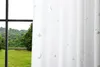 A white curtain with a celestial pattern is shown in front of a window with a view of trees and a body of water. Produktbild-Vorschau