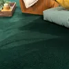 A close-up view of a dark green carpet with a shadow cast across it, suggesting natural light. Produktbild-Vorschau