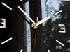 A close-up view of a modern black wall clock with silver hands and red second hand. The clock face has white hour markers and the number '3' is visible. Voir les images du produit