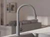 A close-up of a gray kitchen faucet with a blurred background of a living room. Produktbild-Vorschau