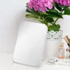 A white makeup mirror is placed on a white surface next to a potted plant and some perfume bottles. Podgląd zdjęcia produktu