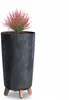A tall, cylindrical planter with a stone-like texture and three wooden legs, holding a small plant with red and green foliage. Anteprima dell’immagine prodotto
