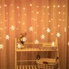 A string of snowflake-shaped LED lights hangs in front of an orange curtain, with a shelf unit visible on the right. Produktbild-Vorschau