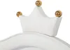 A close-up view of the top of a white bed frame with a crown-shaped headboard adorned with gold balls. Náhľad obrázku produktu