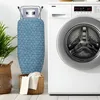 An ironing board is shown standing upright next to a washing machine. Voir les images du produit