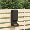 A dark-colored feeder is mounted on a wooden fence, with grass and trees in the background. Anteprima dell’immagine prodotto
