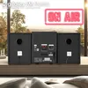 The image shows the back of a Cyberlux compact stereo system with speakers, placed on a wooden surface in front of a window with a blurred outdoor view. Produktbild-Vorschau