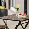 A close-up of a brown rattan-look folding table with two glasses of yogurt and berries on it, with a vase of white flowers in the background. Anteprima dell’immagine prodotto