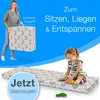 A woman holding a folded mattress and a child playing on an unfolded mattress. Produktbild-Vorschau