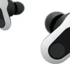 A close-up view of two white and black wireless earbuds against a white background. Produktbild-Vorschau