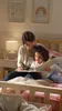 A woman and a child are sitting on a bed, reading a book together. Náhled obrázku produktu