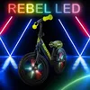 A black balance bike with yellow handlebars and a patterned seat, illuminated by neon lights and reflections on a dark, wet surface. Produktbild-Vorschau