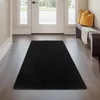 A black rug is placed on a wooden floor in a hallway, leading to a white door with windows. Produktbild-Vorschau