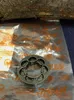 A metal part is placed on a clear plastic bag with orange markings, with a piece of wood in the background. Produktbild-Vorschau