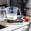 A kitchen scale with a measuring pitcher filled with milk sits on a countertop next to strawberries and a glass of water. Náhľad obrázku produktu