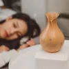 A woman is sleeping in bed next to an essential oil diffuser. Produktbild-Vorschau