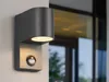 A modern gray outdoor wall light with a motion sensor is mounted on a white wall next to a large window. Produktbild-Vorschau